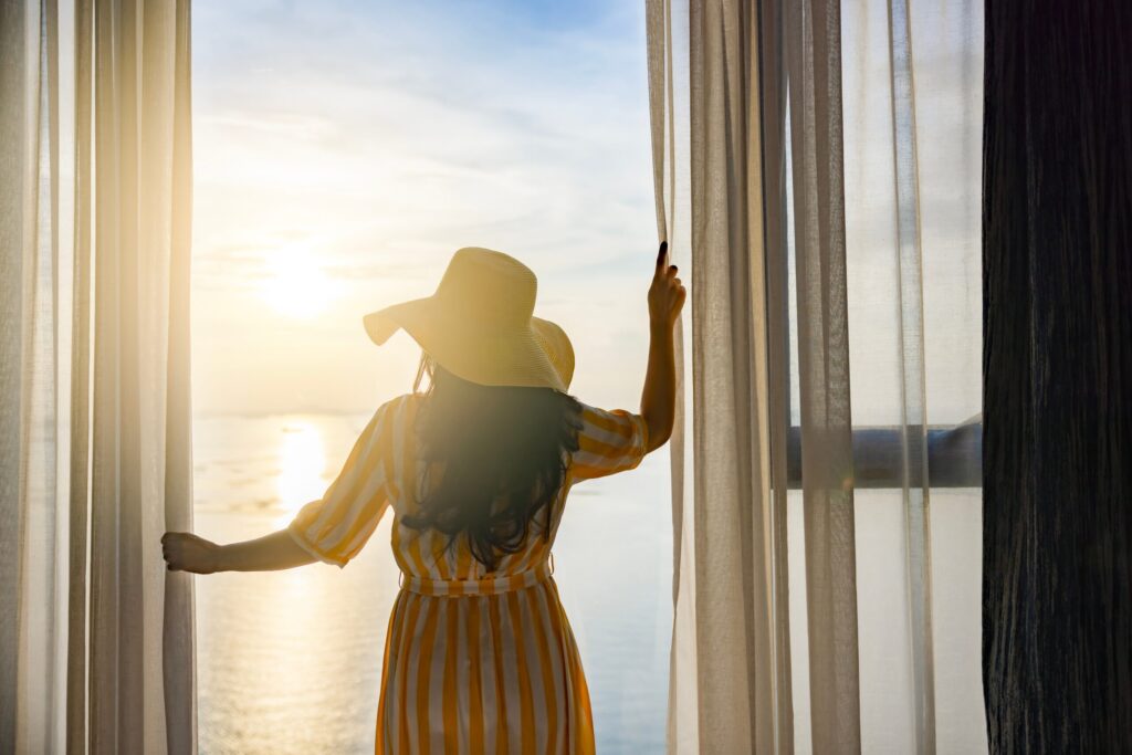 rear,back,view,woman,opening,curtains,,relaxing,and,looking,beautiful